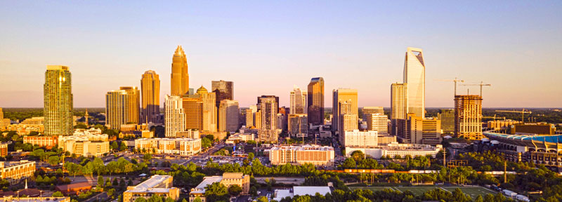 Panoramic view of the Charlotte, North Carolina skyline at sunset with modern skyscrapers and the city skyline glowing in golden light.
