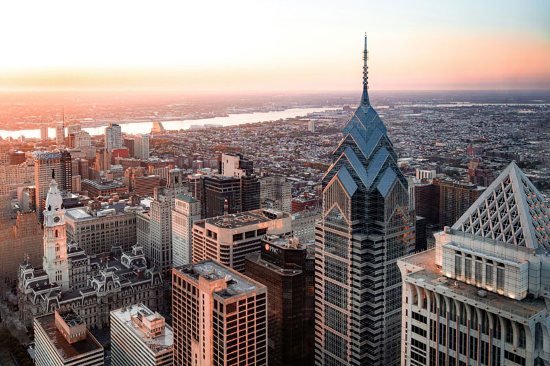 Aerial view of the Philadelphia skyline at sunset featuring Center City skyscrapers and the city stretching toward the horizon.