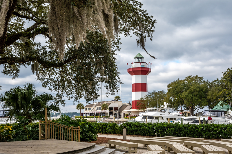 Harbour Town Lighthouse overlooking the marina at Hilton Head Island, framed by oak trees and waterfront docks on a sunny day.