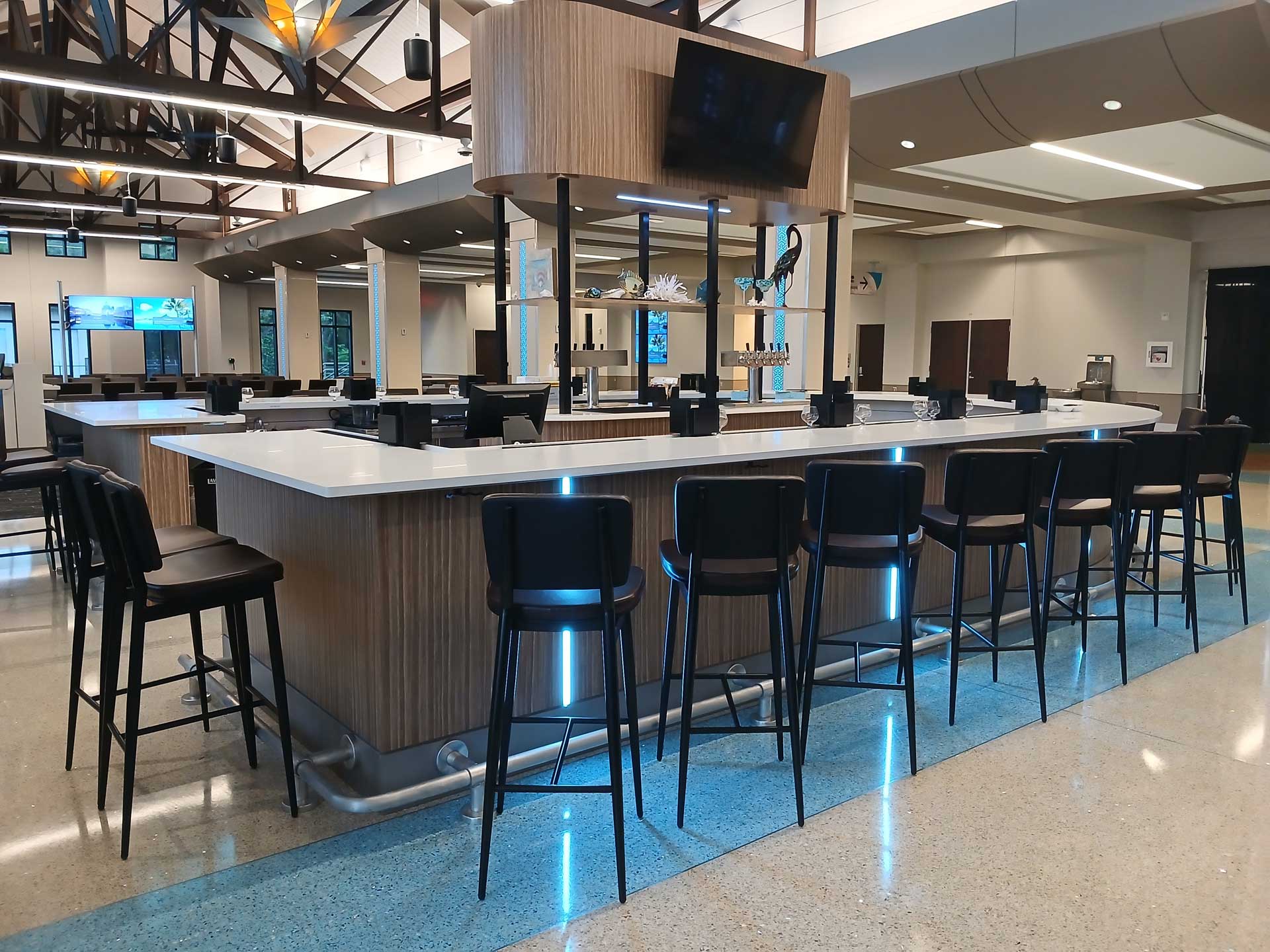 Modern airport bar and lounge area with high-top seating, illuminated counters, and contemporary architectural details.