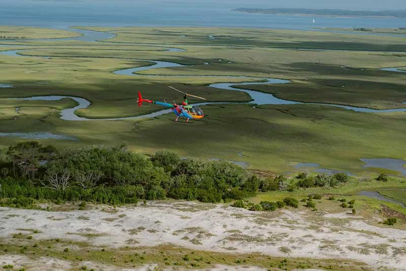 Colorful helicopter flying over the coastal marshes and waterways of the South Carolina Lowcountry on a clear day.