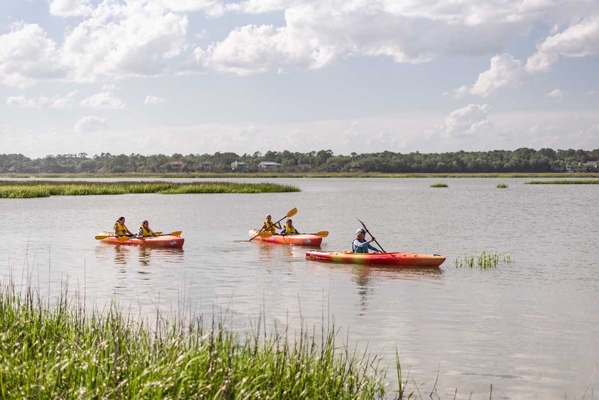 Group of kayakers paddling through a calm Lowcountry marsh surrounded by grasses and coastal waterways.