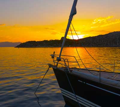 Sailboat anchored on calm water at sunset with golden reflections across the water and a glowing sky.