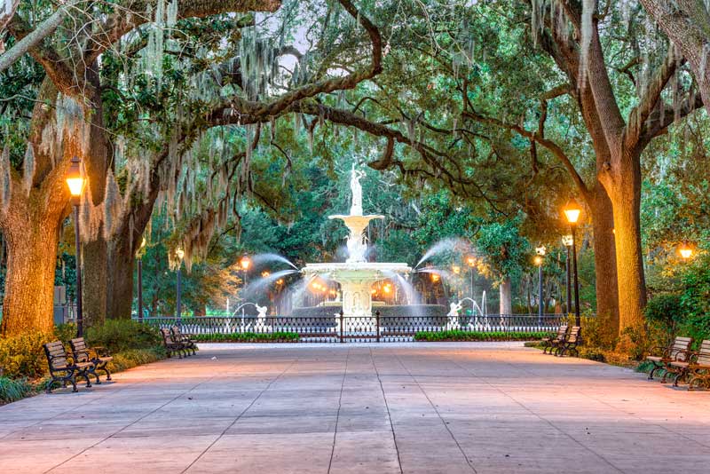 Forsyth Park fountain in Savannah, Georgia, surrounded by oak trees draped in Spanish moss and illuminated by historic streetlights.
