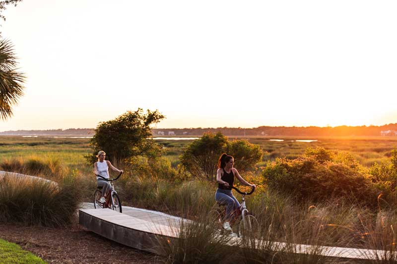 Two people riding bikes on a bike path at sunset