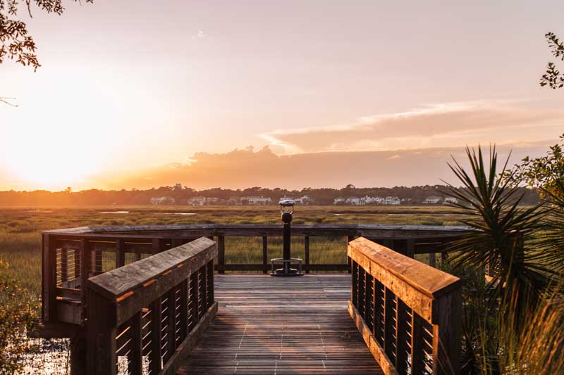 Wooden boardwalk and observation deck overlooking a marsh at sunset.