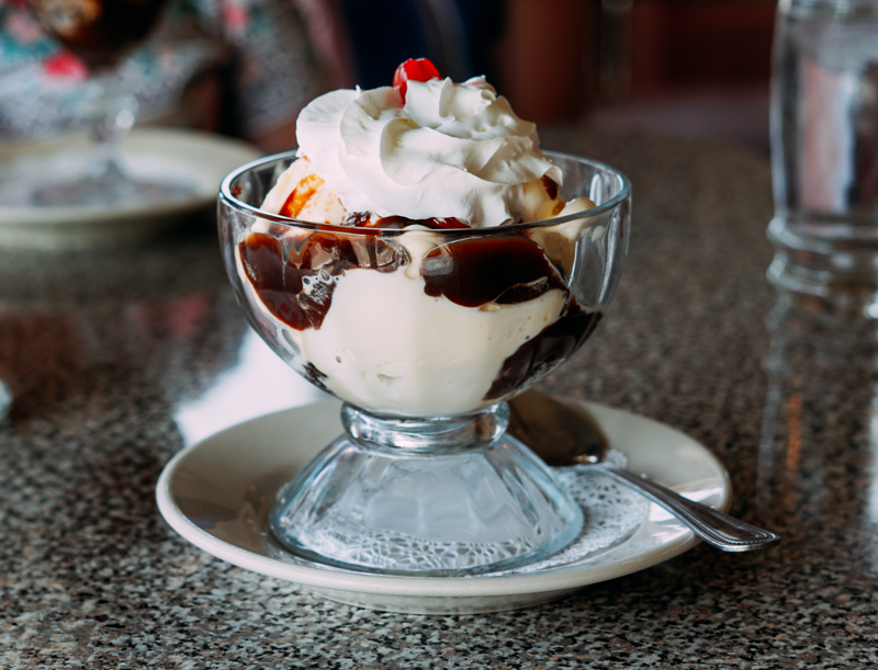 Ice cream sundae with vanilla ice cream, hot fudge, and whipped cream in a glass cup