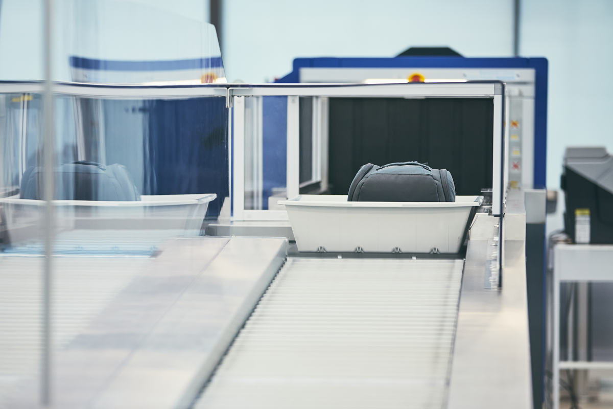 Airport security checkpoint with carry-on luggage moving through an X-ray scanner.